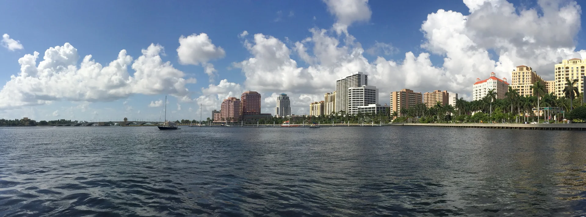 Vista diurna do waterfront de West Palm Beach, com palmeiras, calçadão e céu claro.